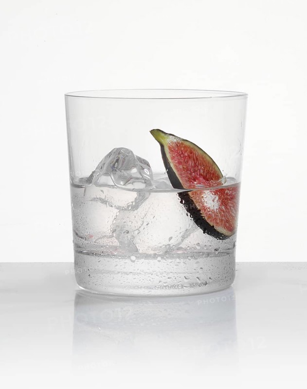 White rum in a tumbler on ice with a fig slice as garnish against a white background, studio shot
