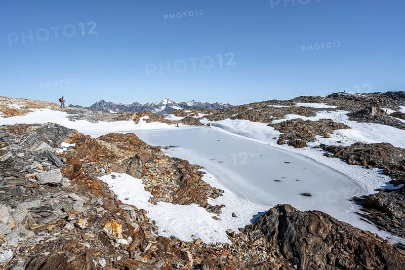 Mountaineer in rocky high mountain landscape, frozen small mountain lake, mountain tour from the Wilder Freiger to the Red Ridge, Stubai Alps, South Tyrol, Italy