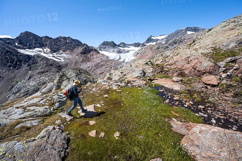 Mountaineer walking over stones, rocky mountain landscape, behind Königshofspitz, Schwarzwandspitz and glacier Ãœbeltalferner, descent from the summit Roter Grat, Stubai Alps, South Tyrol, Italy