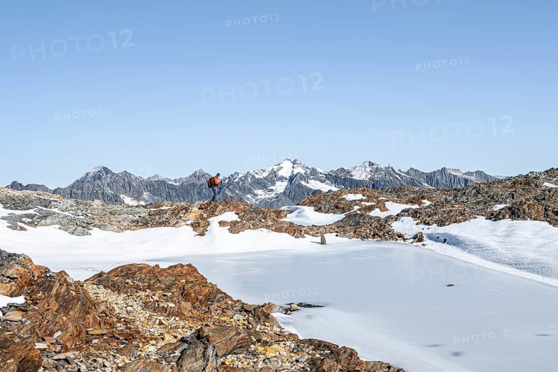Mountaineer in rocky high mountain landscape, frozen small mountain lake, behind mountain peak Ruderhofspitze Mountain tour from the Wilder Freiger to the Red Ridge, Stubai Alps, South Tyrol, Italy