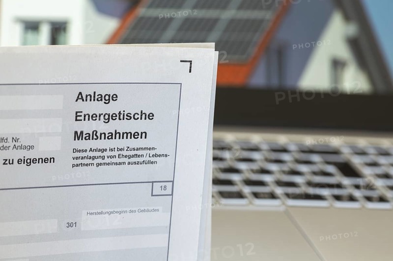 Close-up of tax return, energy measures attachment, in the background a picture of a solar roof on the screen of a laptop