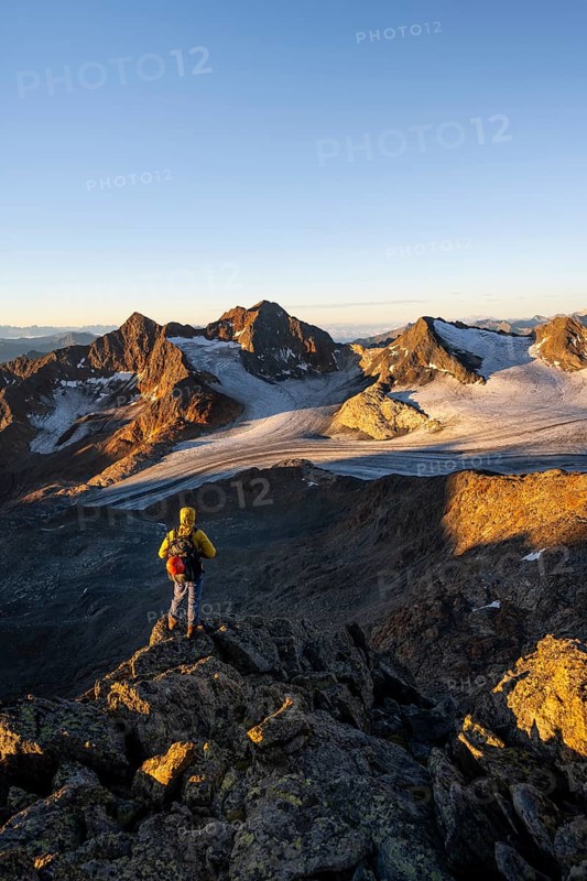 Mountaineers in front of a picturesque high mountain landscape at sunrise with alpenglow, glacier and rocky mountain peaks in the morning light, view at the Becher on mountain peak Königshofspitz and glacier Ãœbeltalferner, Stubai Alps, South Tyrol, Italy