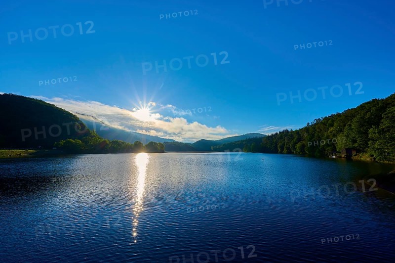 Lake in the morning light with sun, blue sky and surrounding mountains, summer, Rursee, Obersee, Rurberg, Simmerath, Eifel National Park, Eifel, North Rhine-Westphalia, Germany
