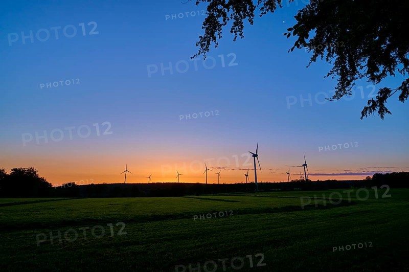 Silhouettes of wind turbines rise into the colourful morning sky as the sun rises behind the meadow, summer, Rohren, Monschau, Eifel, North Rhine-Westphalia, Germany