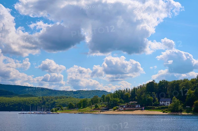 Houses and boats on the shore of a lake, surrounded by green hills under a cloudy sky, summer, Rursee, Rurtalsperre, Simmerath, Eifel National Park, North Rhine-Westphalia, Germany