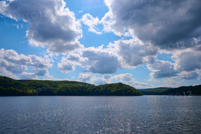 Blue sky with clouds over a calm, glittering lake and wooded hills, summer, Rursee, Rurtalsperre, Simmerath, Eifel National Park, North Rhine-Westphalia, Germany