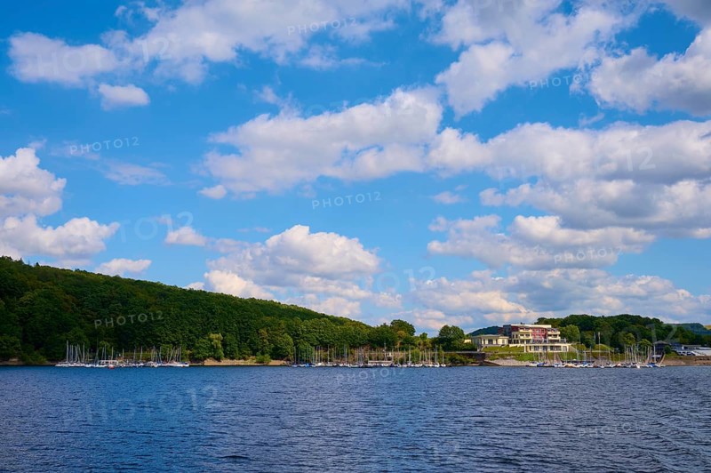 A lake with a building and boats along a wooded shore under a cloudy sky, summer, Rursee, Rurtalsperre, Heimbach, Simmerath, Eifel National Park, North Rhine-Westphalia, Germany