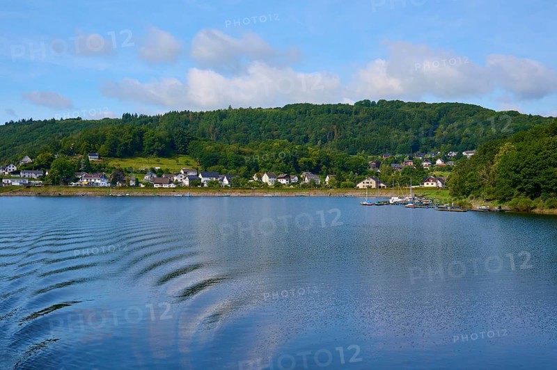View across the lake to a village with hills in the background, Rursee, Rurberg, Simmerath, Eifel National Park, North Rhine-Westphalia, Germany