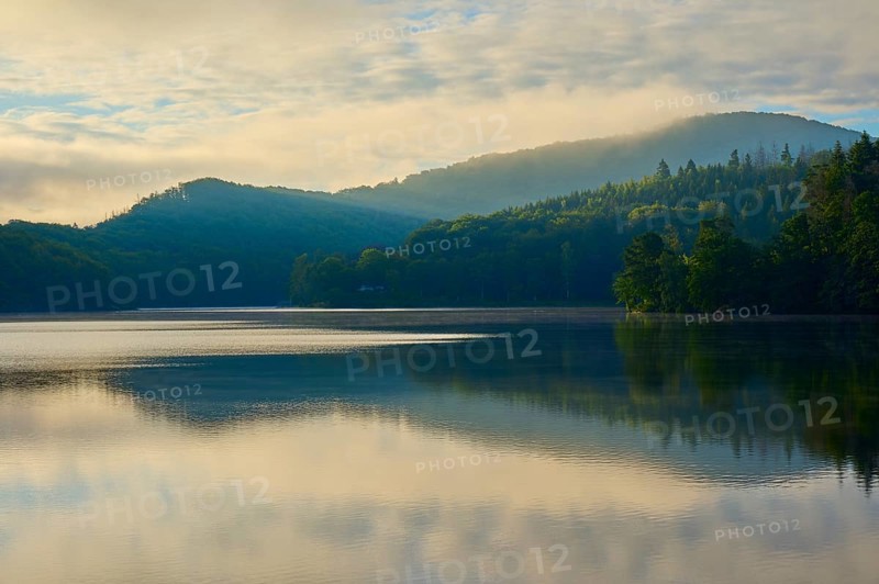 Calm lake with mountains in the background, dense forest and morning sun, gentle mist on the shore, summer, Rursee, Obersee, Rurberg, Simmerath, Eifel National Park, North Rhine-Westphalia, Germany