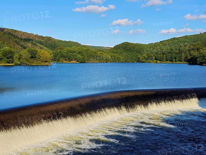 Clear water flows over a dam in a lake surrounded by forests with a blue sky, summer, Rursee, Obersee, Rurberg, Simmerath, Eifel National Park, North Rhine-Westphalia, Germany