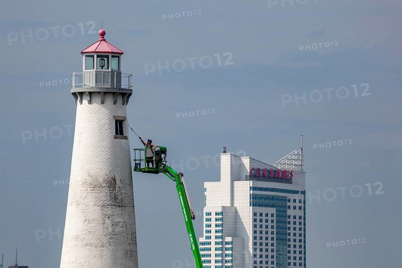 Detroit, Michigan - A worker on a lift paints the Milliken State Park Lighthouse. The lighthouse is on the Detroit River, near downtown Detroit. The Caesars Casino hotel is across the river in Canada