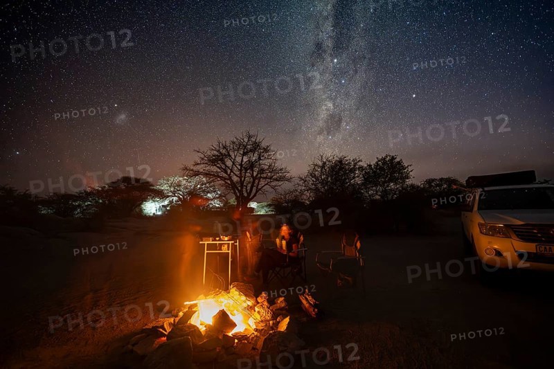 Tourists sitting around a campfire next to their off-road vehicle at night, night shot with starry sky and Milky Way, Kubu Island (Lekubu), Sowa Pan, Makgadikgadi Salt Pans, Botswana