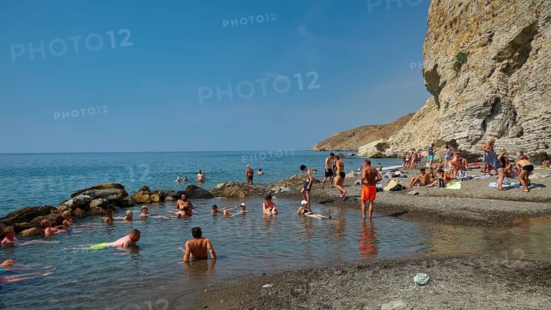 People relaxing on the beach in front of rocky coast and clear blue sea, Embros Thermal Baths, Kos, Dodecanese, Greek Islands, Greece