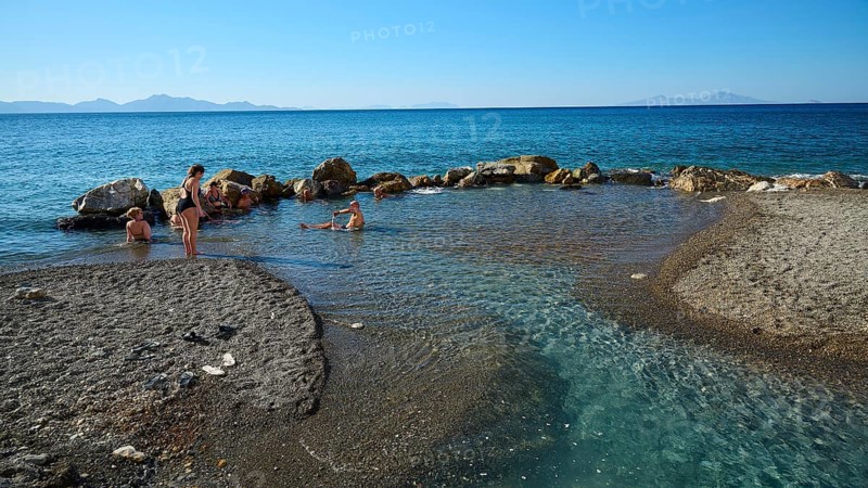 People swimming in the calm blue sea by rocks and sandy shore, Embros Thermal Baths, Kos, Dodecanese, Greek Islands, Greece
