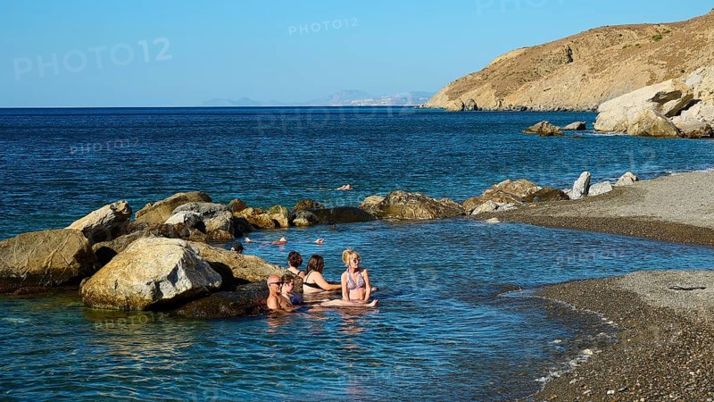 People relaxing in the water on the coast with rocks and clear blue sea, Embros Thermal Baths, Kos, Dodecanese, Greek Islands, Greece