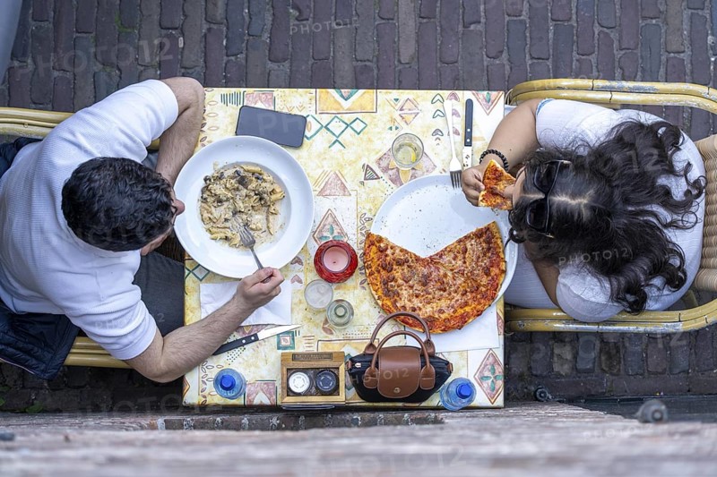 Man and woman sitting in an Italian restaurant eating pizza and pasta, symbolic picture