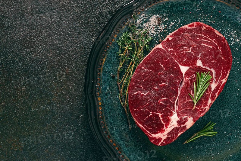 Steak made from fresh beef, with herbs and various spices, on a plate, ready to cook, there are no people