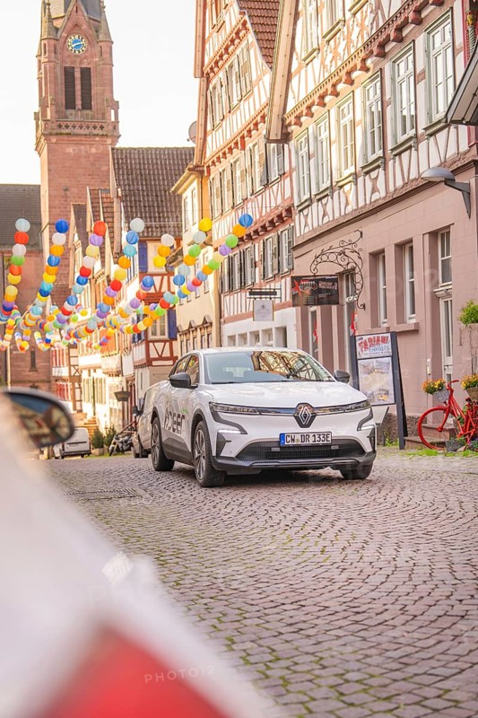 A white electric car parked on a cobbled street decorated with balloons in the old town centre, Deer E, car sharing, electric car, Calw, Black Forest