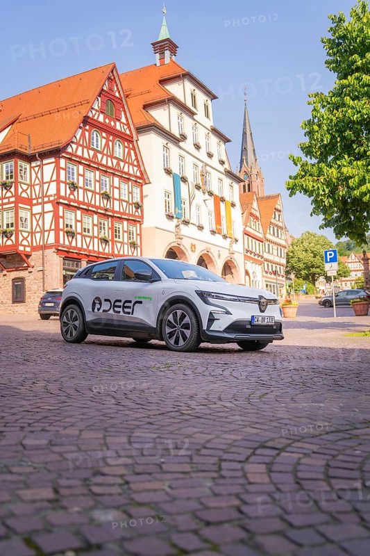 A white car is parked on a cobblestone square next to historic half-timbered buildings with a church tower, Deer E, car sharing, electric car, Calw, Black Forest