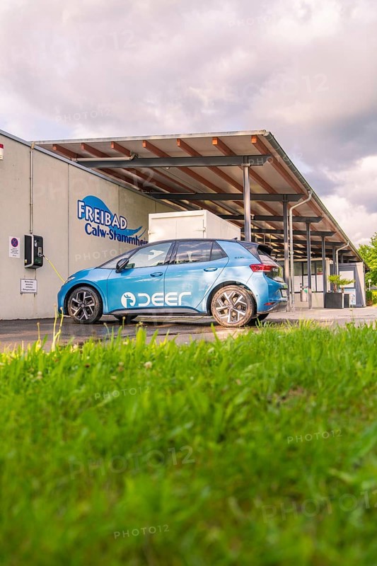 Electric car near an outdoor swimming pool, surrounded by grass and under a cloudy sky, Deer E, car sharing, electric car, Calw, Black Forest