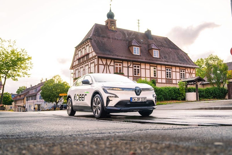 A white electric car drives past a traditional building in a historic town, Deer E, car sharing, electric car, Calw, Black Forest