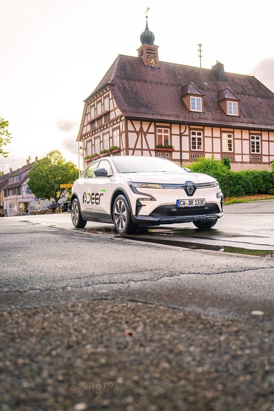 A white electric car parked in front of a traditional building with a bell tower in an old town, Deer E, car sharing, electric car, Calw, Black Forest