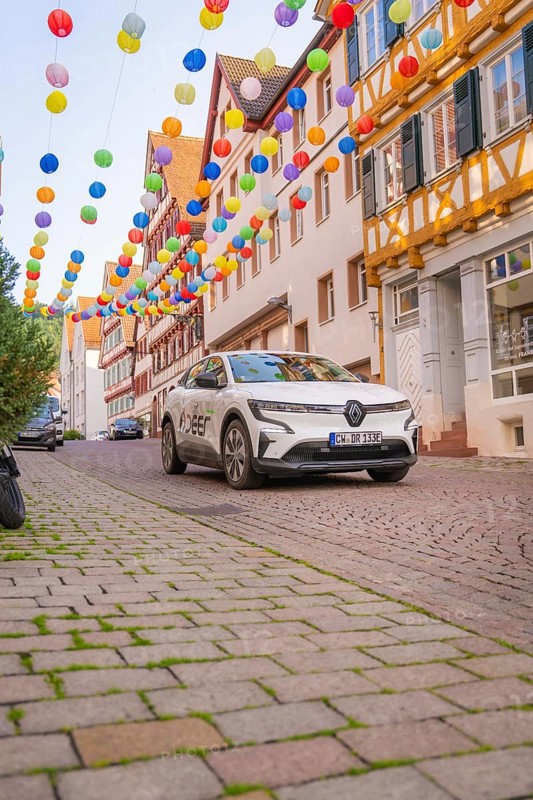 A car drives under colourful garlands in a cobbled street, Deer E, car sharing, electric car, Calw, Black Forest