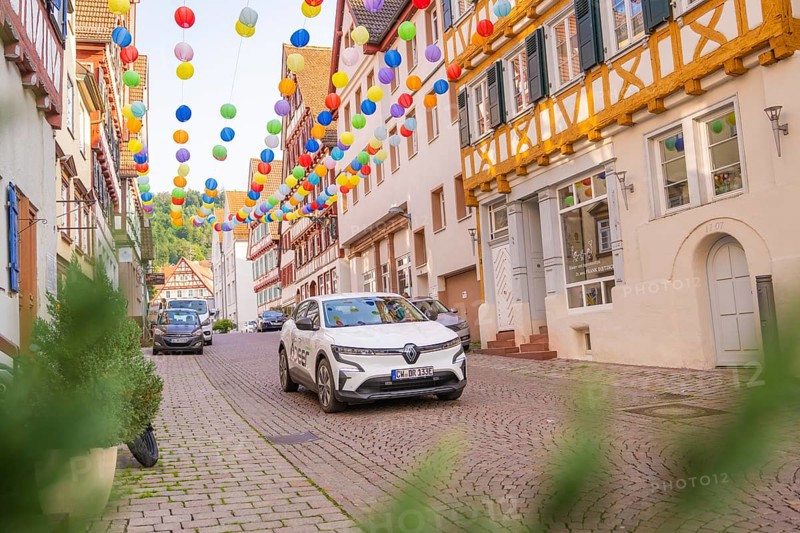 A car drives through a street decorated with colourful garlands in an old town, Deer E, car sharing, electric car, Calw, Black Forest