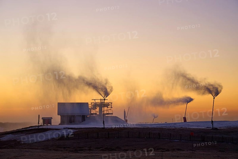 Snow cannons blow clouds of smoke on a hilltop under the purple twilight sky, winter, Route de Cretes, Hohneck, La Bresse, Vosges, France