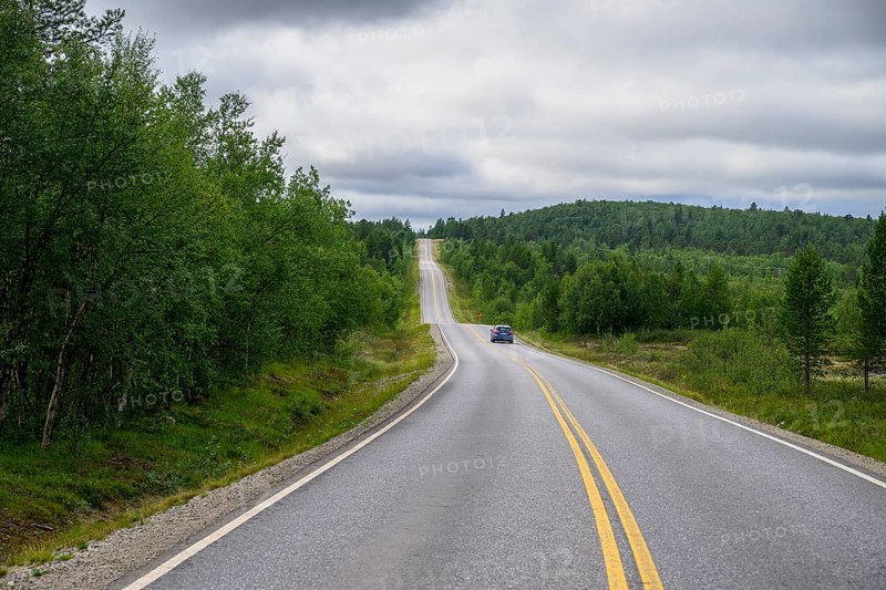 A lonely road leading through a green, wooded hilly landscape of Finland's countryside, Karelia, Lapland, Finland