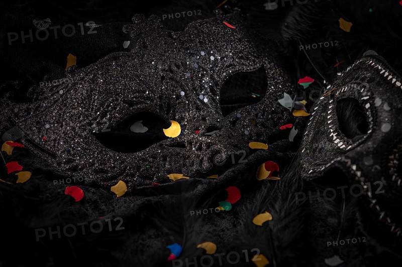 Black mask with confetti on dark background, contrasting carnival atmosphere