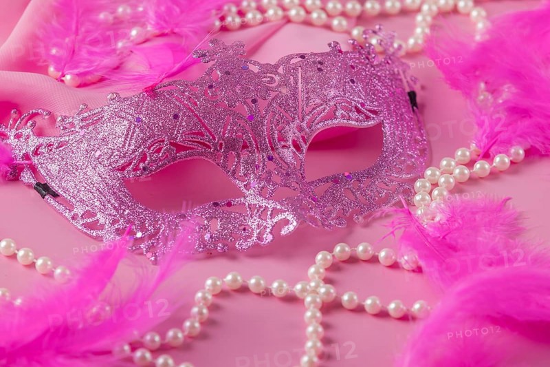 Glittering pink mask on pink background with feathers and pearl necklaces