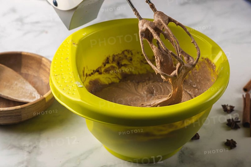 Electric mixer processes cocoa dough in a yellow bowl