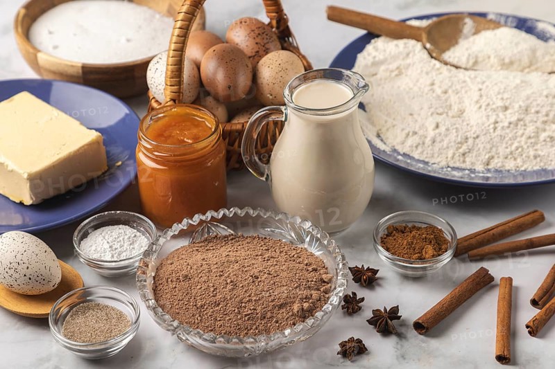 Baking ingredients, flour, sugar, cinnamon, milk, butter, cocoa, jam and eggs on a table
