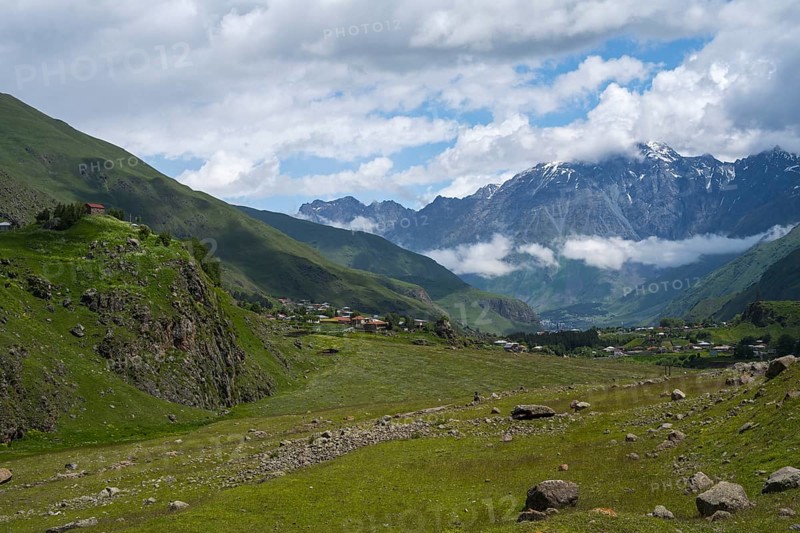 A wide valley stretches against snow-capped mountain peaks under a cloudy sky, Kazbegi, Qasbegi, Stepantsminda, Georgian Military Highway, Mtskheta-Mtianeti province, Mount Shani in the background, located in Ingushetia, Russia, High Caucasus, Georgia