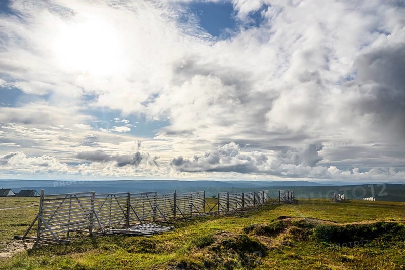 Landscape with vast sky and clouds bounded by a protective fence against snowdrifts Wooden fence along an open area, Kaunispää Caabuaivas, Lapland, Finland