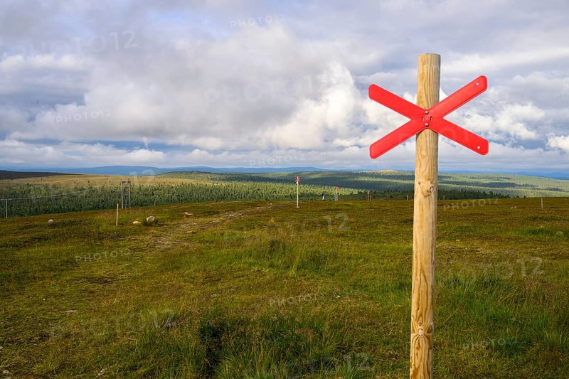 Red snowmobile snowscooter marker on a wooden post in front of a vast landscape under clouds, Kaunispää Caabuaivas, Lapland, Finland