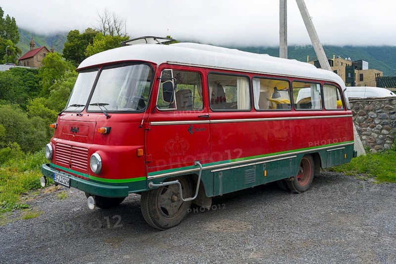 Red retro bus with green stripes on a road in a rural mountain landscape, vintage car, Robor LO 3000 bus from the GDR, Georgia