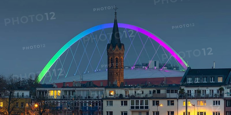 Evening view of residential buildings on the banks of the Rhine, behind them the church tower of St. John's Church and the rainbow illuminated arch of the Lanxess Arena, Cologne-Deutz, Cologne, North Rhine-Westphalia, Germany