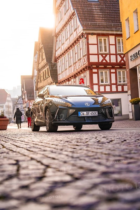 Car drives through an old town with half-timbered houses, some people on foot, MG4 electric car, deer e-car sharing, Calw, Germany