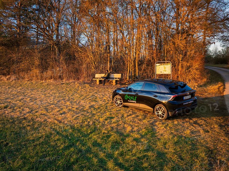 Car parked in rural landscape with benches at sunrise, surrounded by trees, MG4 electric car, deer e-car sharing, Calw, Germany