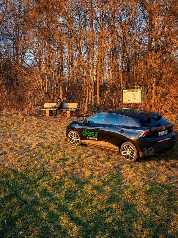 Black car parked on the edge of a forest next to a bench at sunset, MG4 electric car, deer e-car sharing, Calw, Germany