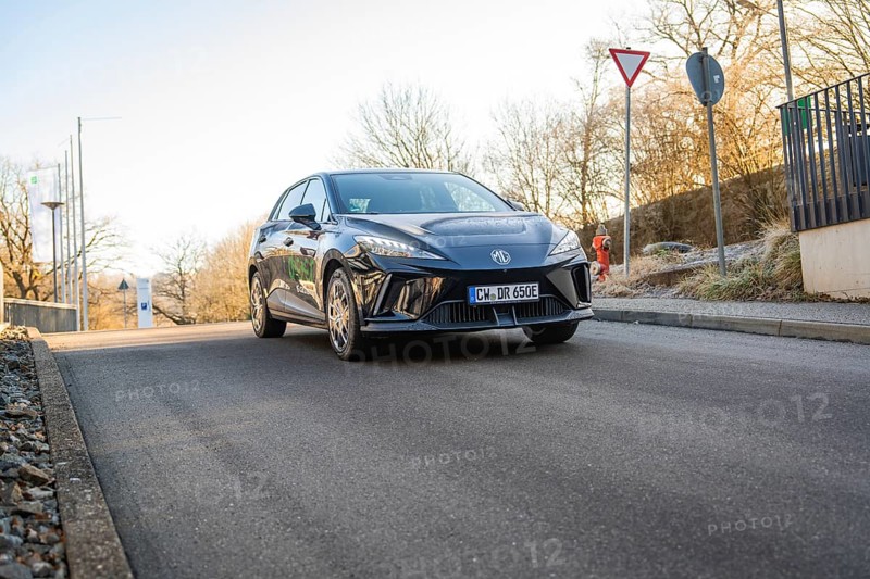 A black car at a junction surrounded by trees and road signs in sunlight, MG4 electric car, Deer e-Carsharing, Calw, Germany