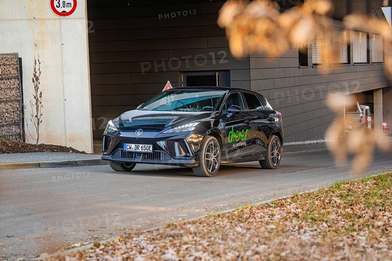 Car parked near a modern building, autumnal atmosphere due to falling leaves, MG4 electric car, deer e-car sharing, Calw, Germany