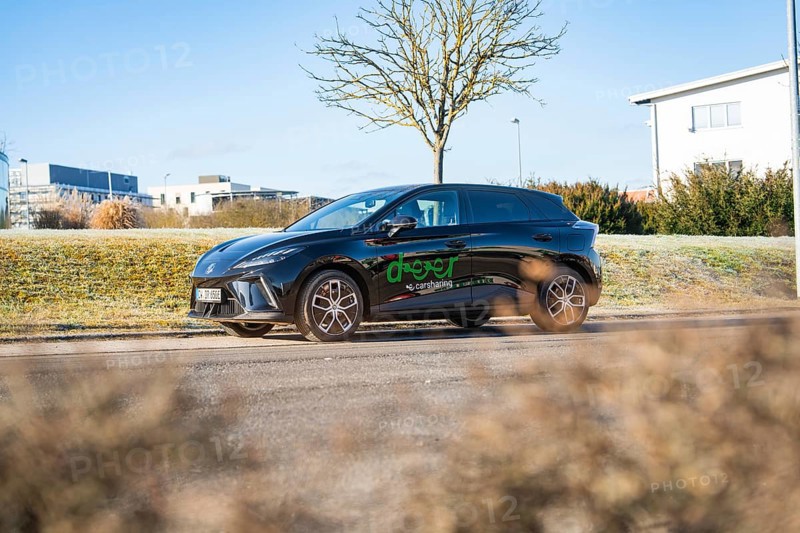 Black car driving along a wintry landscape with modern buildings in the background, MG4 electric car, Deer e-Carsharing, Calw, Germany