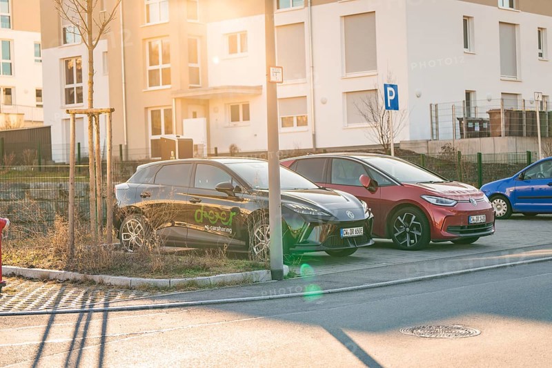 Two electric cars in a parking lot in front of residential buildings, in the warm light of the setting sun, MG4 electric car, Deer E-Carsharing, Calw, Germany