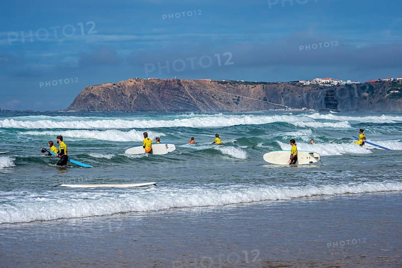 Participants in a surfing course go into the water, beach Praia de Vale Figueiras, village Arrifana in the back, western Algarve, Portugal
