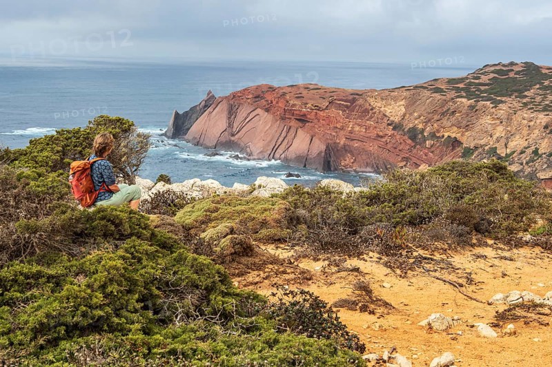 Hiking woman takes a break, view over cliff, Fishermens Trail, Rosa Vicentina, western Algarve just north of cape Cabo de Sao Vicente, Portugal
