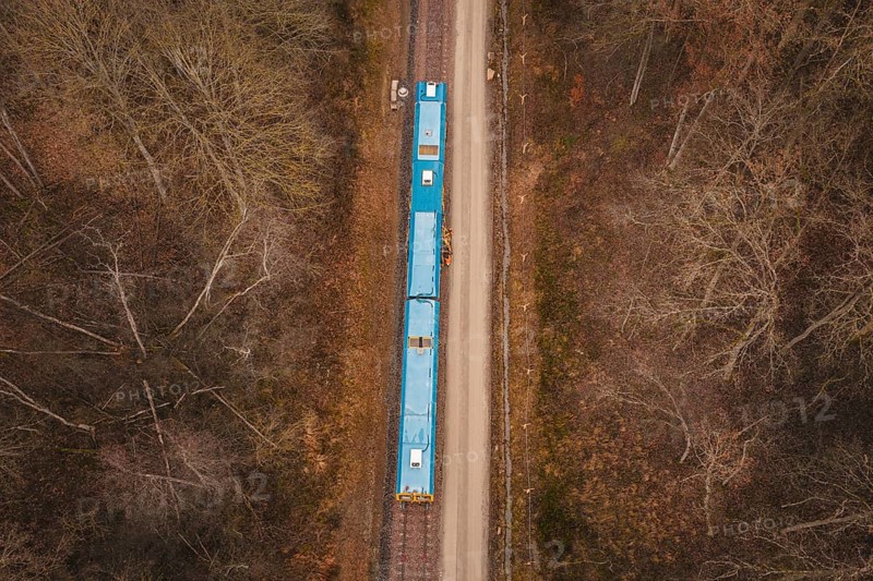Bird's-eye view of railway line with yellow train in a wooded region, using a tamping machine at the Hermann Hessebahn construction site, Calw, Germany
