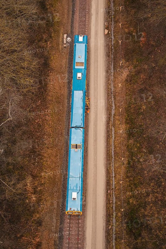 Aerial view of a yellow train on a construction site in a wooded area, using a tamping machine at the Hermann Hessebahn construction site, Calw, Germany